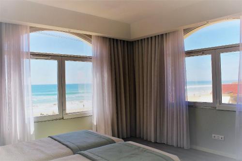 a bedroom with a bed and windows with a view of the beach at Golden Beach Guest House & Rooftop Bar in Faro