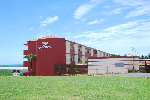 a red and white building with a grass field at Hotel Murasakimura in Yomitan