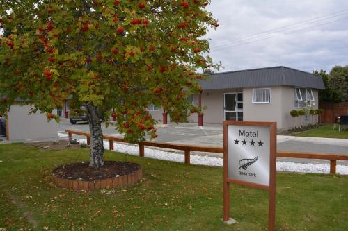 a sign in front of a tree with red flowers at Amber Court Motel in Te Anau