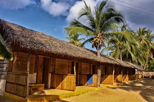a building with a straw roof with palm trees at Sandy Edge in Kalpitiya
