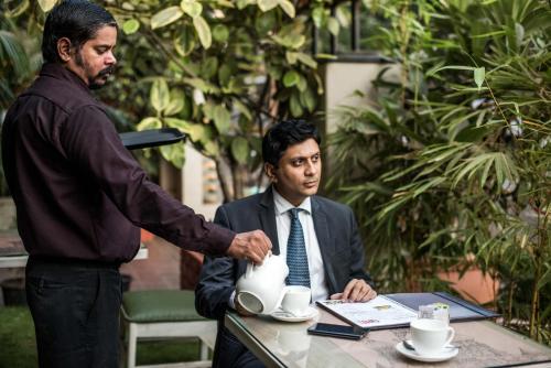 two men sitting at a table with a man holding a tea pot at Hotel Oriental Aster - Mumbai International Airport in Mumbai