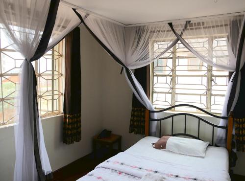 a bedroom with a canopy bed and two windows at Hotel Acacia City in Kampala