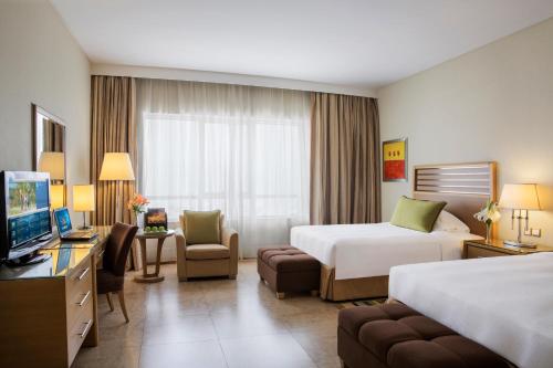 a hotel room with two beds and a television at Nour Arjaan by Rotana-Fujairah in Fujairah