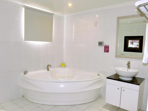 a white bathroom with a large tub and a sink at Huang Xing Motel in Pingtung City