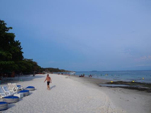 a man walking down a beach with chairs and people at Runa Runa The Best Samed Island in Ko Samed
