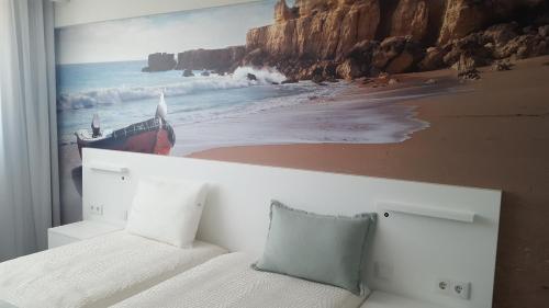 a bedroom with a painting of a boat on the beach at Golden Beach Guest House & Rooftop Bar in Faro