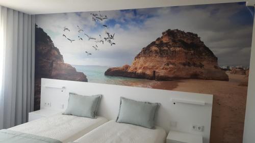 a bedroom with two beds and a painting of a beach at Golden Beach Guest House & Rooftop Bar in Faro