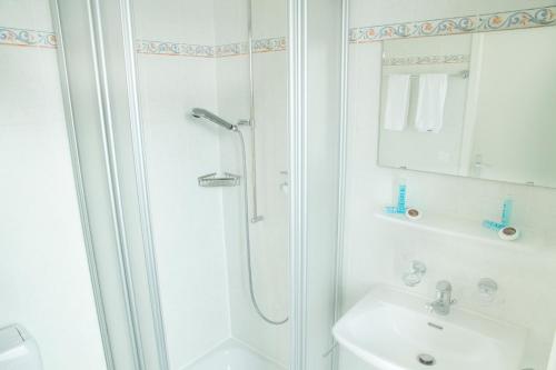 La salle de bains blanche est pourvue d'une douche et d'un lavabo. dans l'établissement Résidence de l'Ours, à Lausanne