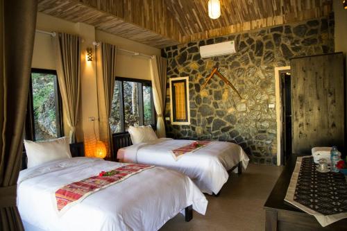 a bedroom with two beds and a stone wall at Mai Chau Moment Spa & Resort in Mai Chau