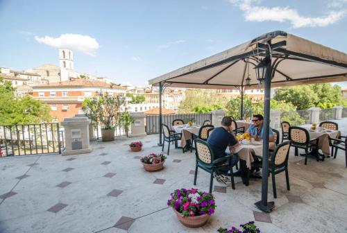 two people sitting at tables under an umbrella on a patio at Hotel Iris in Perugia
