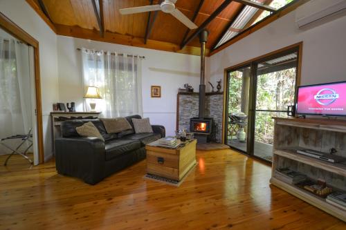 a living room with a couch and a tv at Crater Lakes Rainforest Cottages in Yungaburra