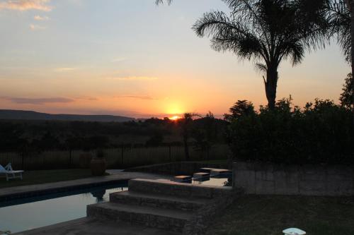 a sunset over a swimming pool with a palm tree at Country Park Guest House - Muldersdrift in Muldersdrift