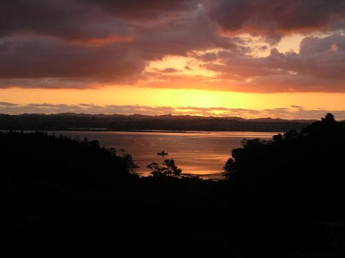 a sunset over a lake with a boat in the water at Fernglen B&B in Auckland