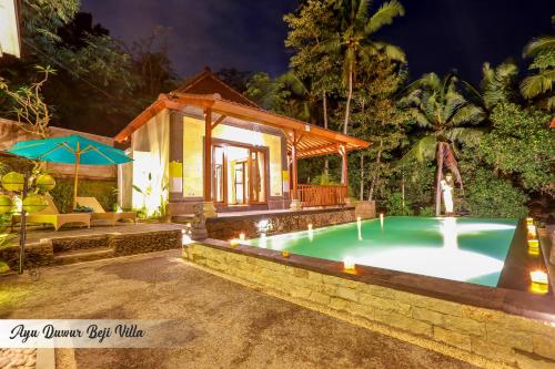 a swimming pool in front of a villa at night at Ayu Duwur Beji in Ubud