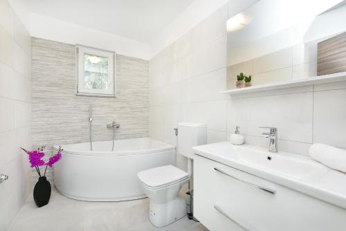 a white bathroom with a tub and a toilet and a sink at Apartman Kresan in Sukošan