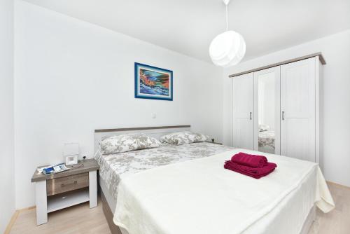 a white bedroom with a bed with a red object on it at Apartman Kresan in Sukošan