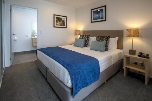 a bedroom with a large bed with a blue blanket at Ramada Suites by Wyndham Albany in Auckland