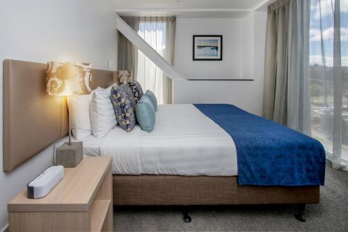 a bedroom with a bed and a desk and a window at Ramada Suites by Wyndham Albany in Auckland