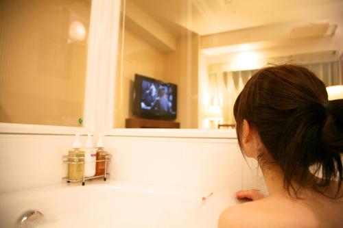 a woman sitting in a bathroom looking at a mirror at Hotel Boston Plaza Kusatsu in Kusatsu