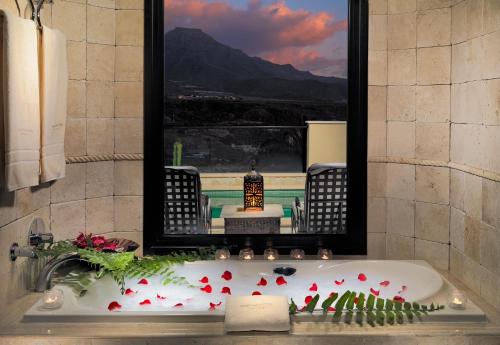a bathroom with a bath tub with red flowers and a mirror at Royal Garden Villas, Luxury Hotel in Adeje