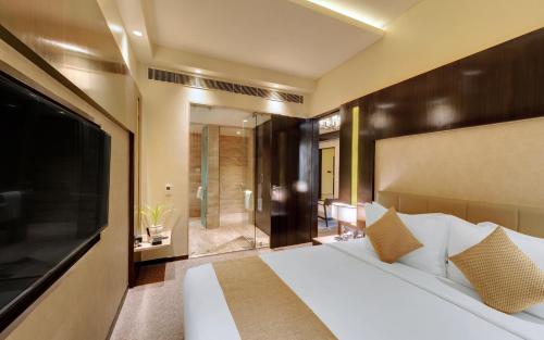 1 dormitorio con 1 cama blanca grande y TV en Iscon The Fern Resort & Spa, Bhavnagar en Bhavnagar