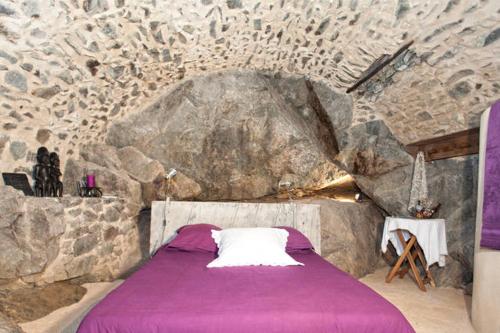 a bedroom with a purple bed in a stone wall at Chez Caro in Corbara