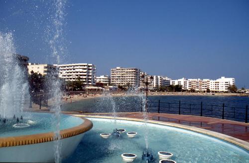 a fountain in a pool next to a beach with buildings at Hostal y Apartamentos Santa Eulalia in Santa Eularia des Riu