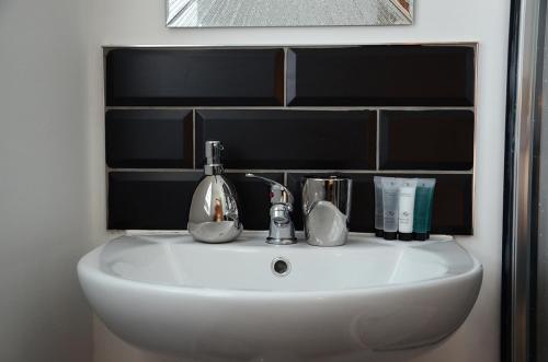 a white bathroom sink with a black tile wall at Frankies Wine Bar & Lodge in Disley