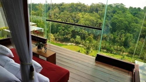 a room with a large window looking out at a forest at Ayuterra Resort in Ubud