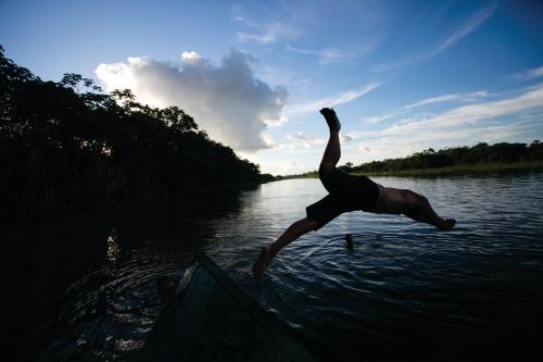 a man is jumping off of a boat in the water at Ämak Iquitos Ecolodge - All Inclusive in Santa Clara