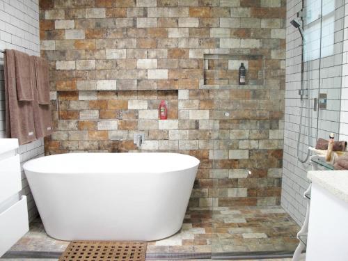 a white tub in a bathroom with a brick wall at Apple Tree Cottage in Mittagong