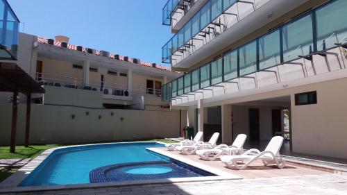 a swimming pool with lounge chairs next to a building at Manawa Beach Flats Prime in Porto De Galinhas