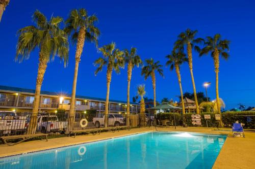 a pool in front of a hotel with palm trees at Brawley Inn in Brawley