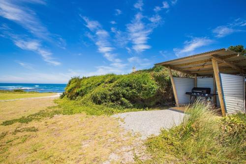 um barracão com um banco ao lado de uma praia em Cottages for Couples em Port Fairy