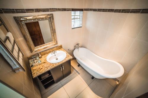 a bathroom with a sink and a mirror and a tub at AnnVilla Guesthouse in Klerksdorp