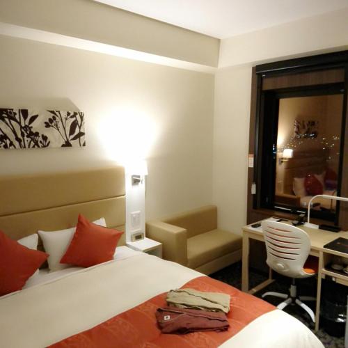 a hotel room with a bed and a desk and a lamp at Queens Hotel Chitose in Chitose