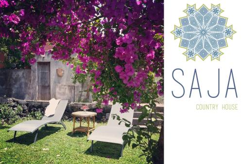 two chairs and a table in a yard with purple flowers at Saja Country House in Acireale