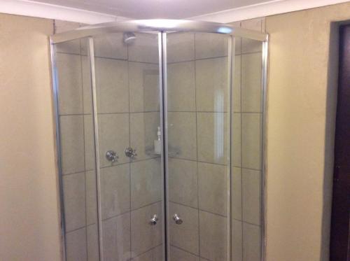 a shower with a glass door in a bathroom at Klein Paradys Lodge - Polokwane in Polokwane