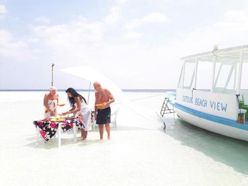 a group of people standing on the beach next to a boat at Detour Beach View in Hangnaameedhoo