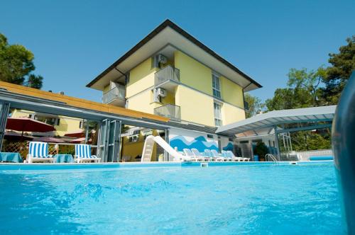 a swimming pool with chairs and a building at Hotel Ai Pini in Grado