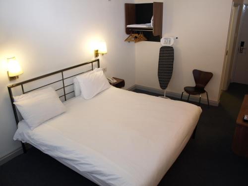 a bedroom with a large white bed and a chair at 247Hotel in Oldham