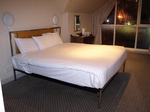 a bedroom with a large bed with white sheets and a window at 247Hotel in Oldham