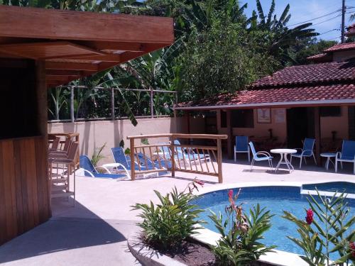 una piscina con sillas, una mesa y una casa en Pousada Mareilha, en Ilhabela