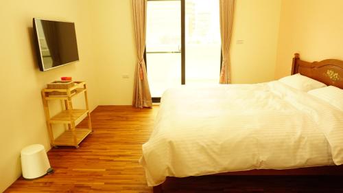 a bedroom with a white bed and a television at Warm Home in Taitung City