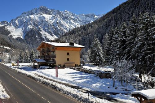 a building on the side of a road with snowy mountains at Hotel Garni Pegrà in Ponte di Legno