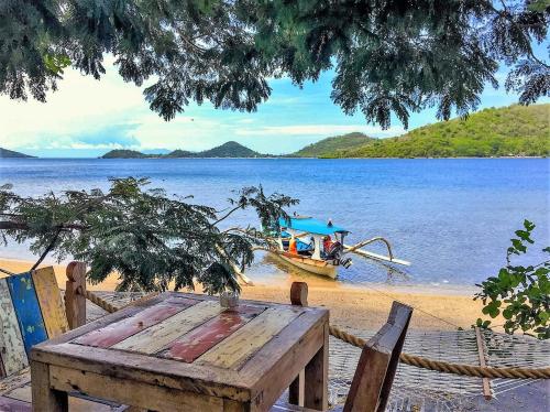 a picnic table on the beach with a boat on the water at Palmyra Indah Bungalows in Sekotong