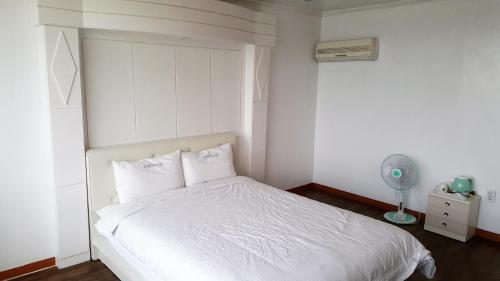 a bedroom with a white bed and a fan at Namhae Beach Hotel in Namhae