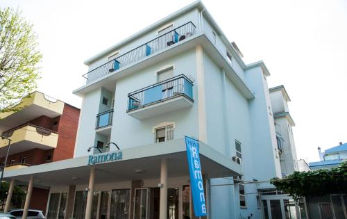 a white building with a blue sign in front of it at Hotel Ramona in Rimini