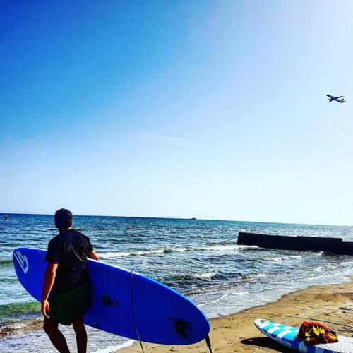 a man walking on the beach holding a blue surfboard at Garden Art in Pervolia