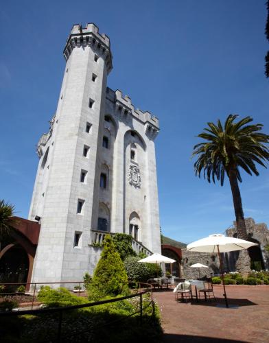 a building with a clock tower with a palm tree at Hotel Castillo de Arteaga in Gautegiz Arteaga